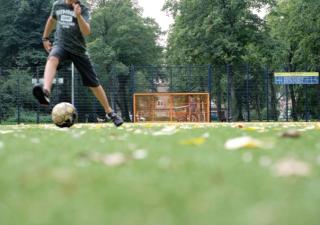 Het Cruijff Court; een groen voetbalveld met een oranje metalen doel waarop een jongen aan het voetballen is