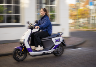 Foto van een vrouw die breed lachend op een deelscooter rijdt