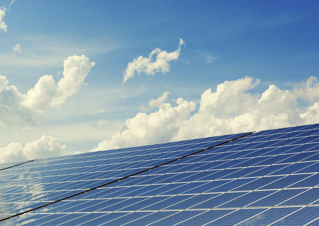 Twee grote zonnepanelen met daarachter een zomerse blauwe lucht met wat witte wolken