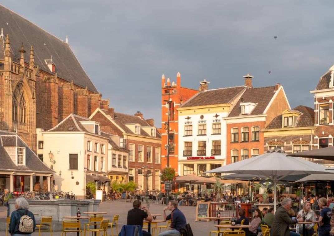 Een plein met verschillende terrassen waar mensen aan tafeltjes zitten. OP de achtergrond staan oude gebouwen