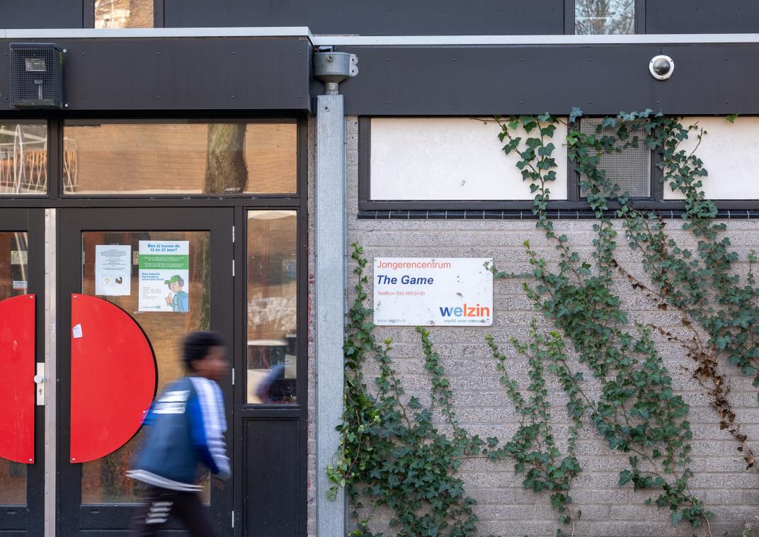 Een jongen loopt voor de ingang van een gebouw