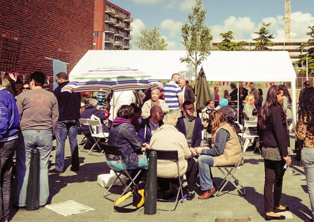 Een groep buurtbewoners buiten onder en rondom een partytent met elkaar in gesprek.