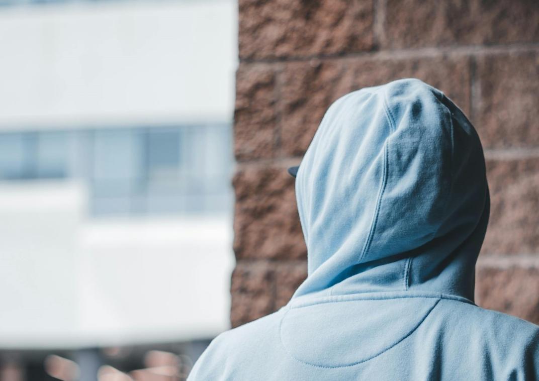 Een jongere met een hoody aan en de capuchon over zijn hoofd, staat met zijn rug naar ons toe