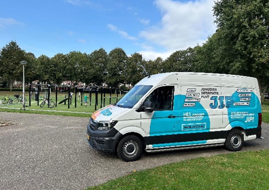 Een wit met blauwe bus staat naast het park.