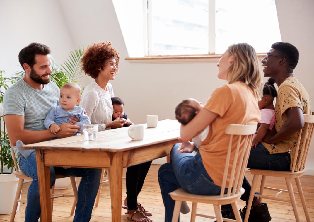 Vier volwassenen zitten aan een tafel met kinderen op schoot.