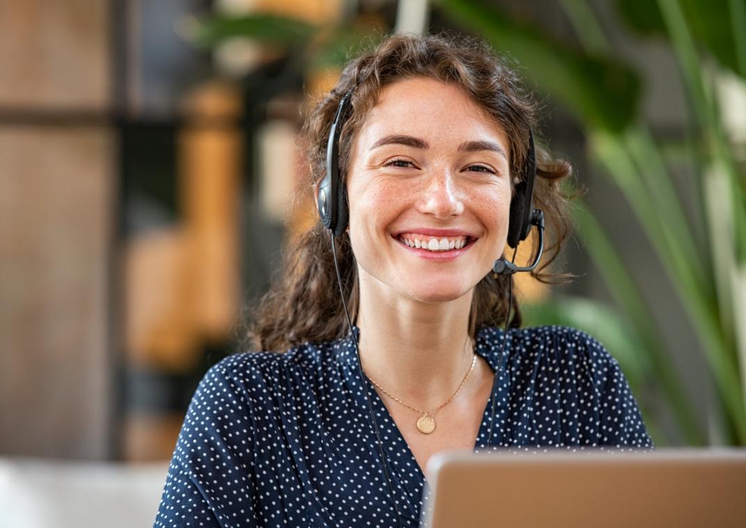 Vrouw achter laptopscherm met headset op.