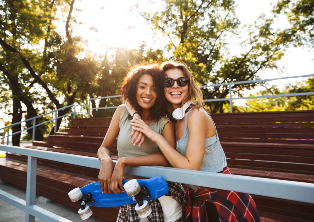 Twee jonge vrouwen staan buiten met een skateboard in hun hand.