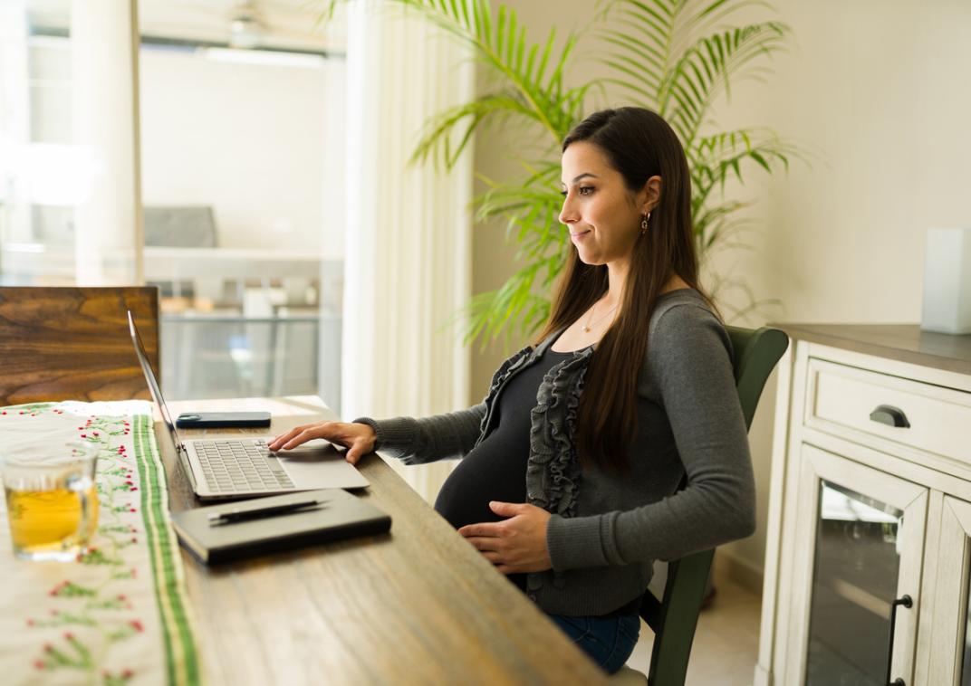 Zwangere vrouw houdt haar buik vast en zit achter een laptop