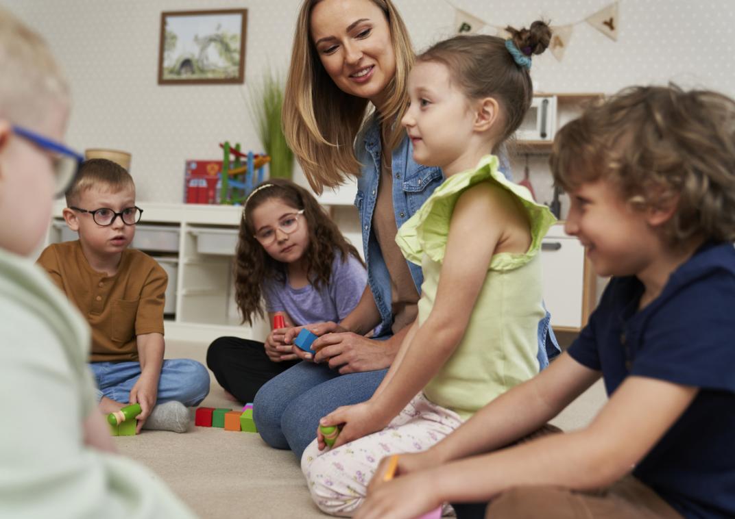 Kinderen zitten in een kring op de grond met een vrouw.