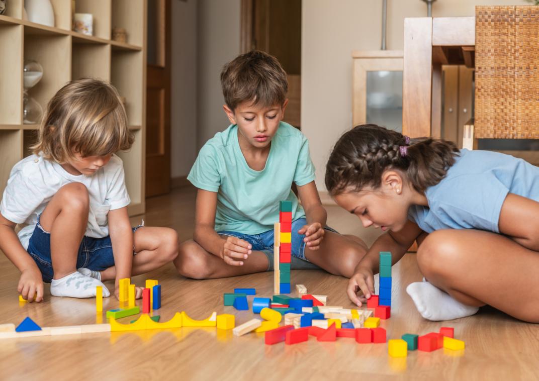 Drie kinderen zitten op de grond te spelen met blokken.