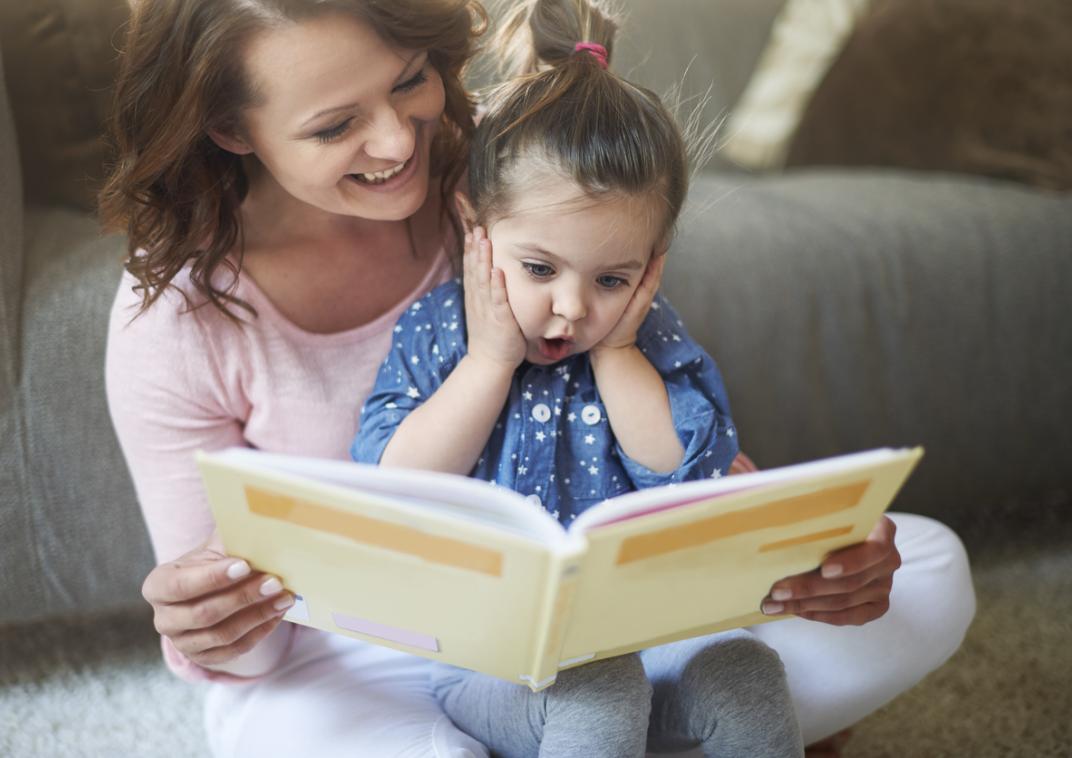 Kind zit op schoot bij een vrouw die een boek voorleest.