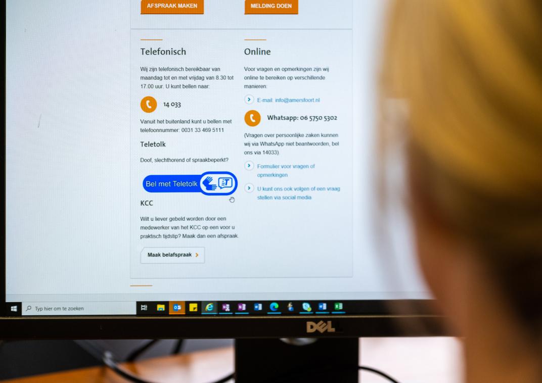 Achterhoofd van een vrouw die naar een beeldscherm van een computer kijkt. Op het beeldscherm van de computer staat een webpagina open met contactgegevens van Gemeente Amersfoort.