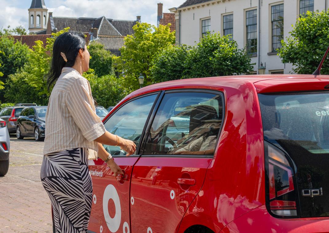 Een vrouw stapt in een rode deelauto.