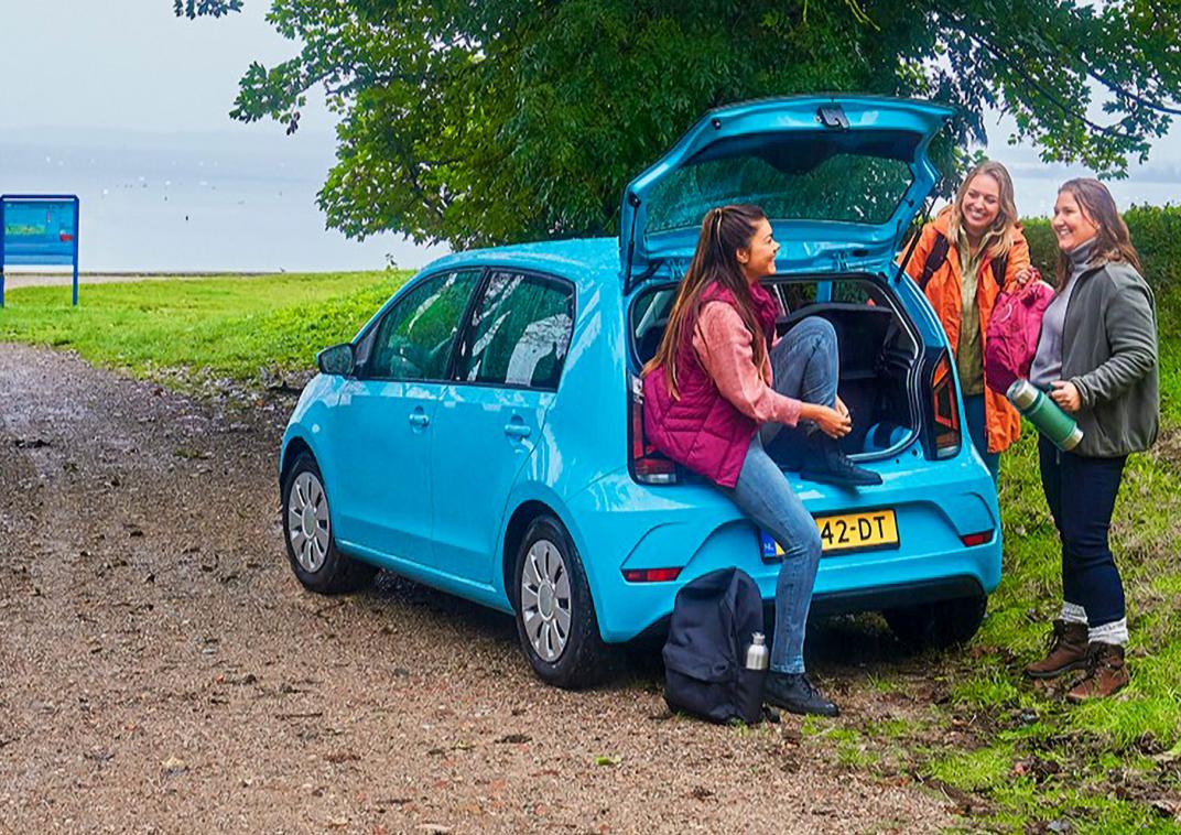 Drie jongeren staan bij een auto.
