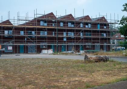 Nieuwbouwwoningen in aanbouw, de muren staan, maar de daken liggen er nog niet op en er staan stellingen tegenaan.