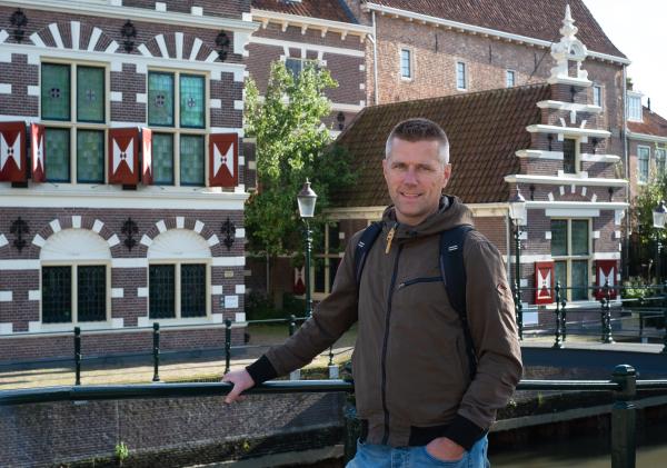 vriendelijk kijkende man bij middeleeuwse gevel en brug