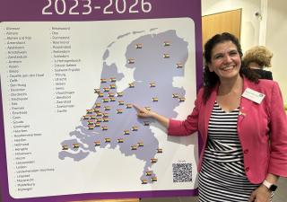 Foto van Wethouder Micheline Paffen-Zeenni bij een kaart van Nederland met daarop aangegeven de regenboogsteden
