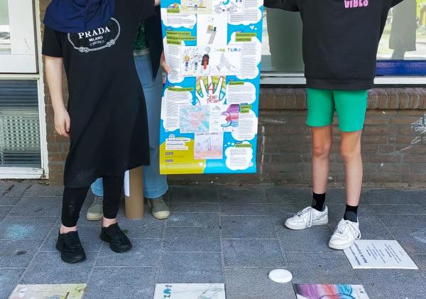 Een juf en twee leerlingen houden een groot papier vast met daarop de tien stappen. In de tegels waar ze op staan is een hinkelbaan verwerkt met daarop ook de tien stappen.