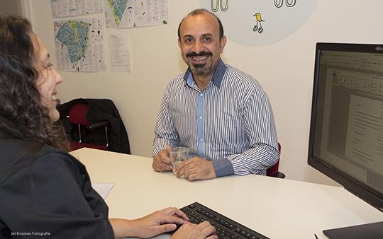 Een breed glimlachende man, zitten aan het bureau van een medewerker