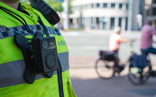 Een handhaver die een Bodycam draagt met op de achtergrond twee fietsers