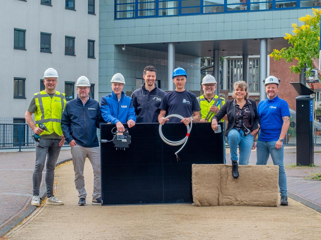 De Makers; zeven mannen en een vrouw die poseren met bouwhelmen op terwijl ze diverse verduurzamende materialen vasthouden