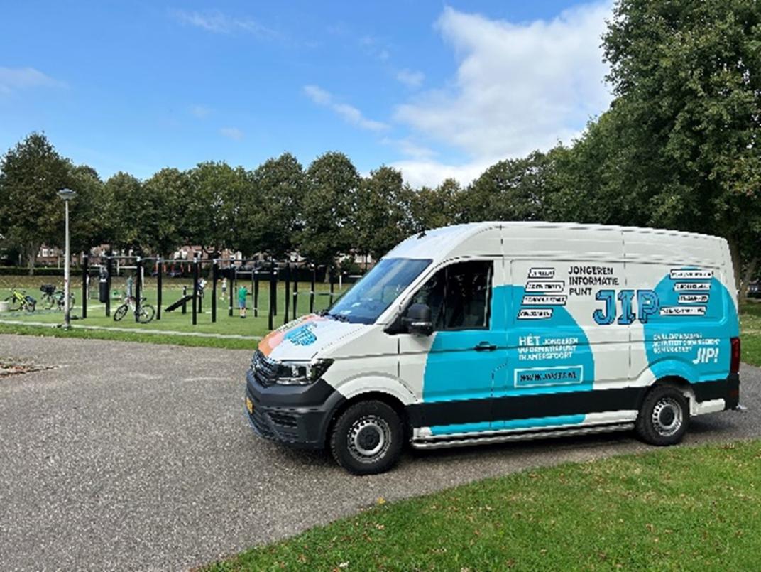 Een wit met blauwe bus staat naast het park.