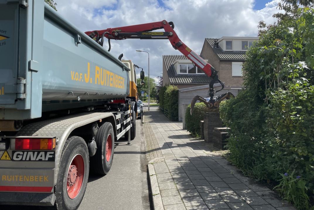 Een vrachtwagen met een bak en een grijparm die een stapel tegels op gaat pakken.