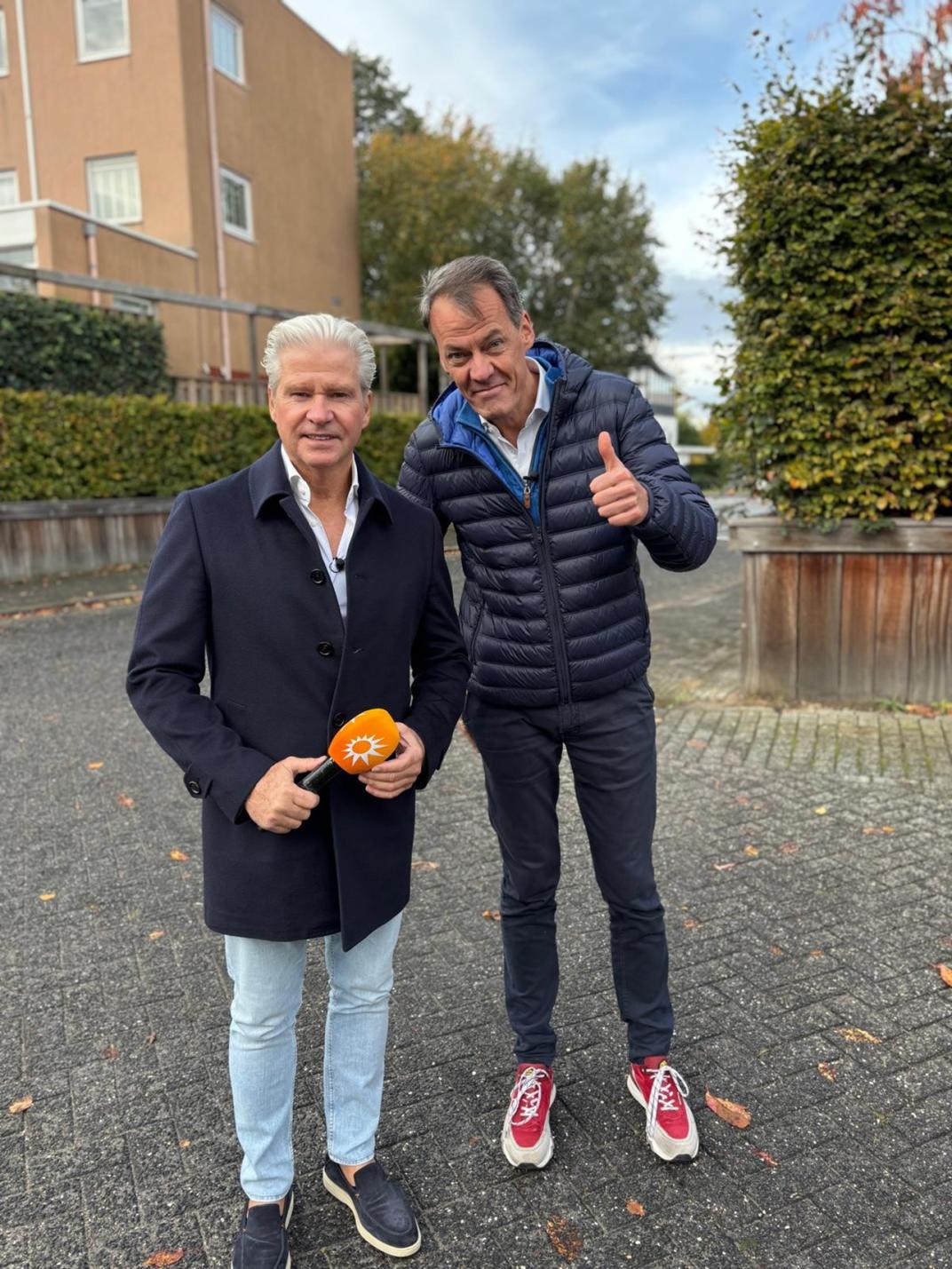 Dries Roelvink houdt een microfoon vast en hij staat naast Amersfoorter Tijs van den Brink