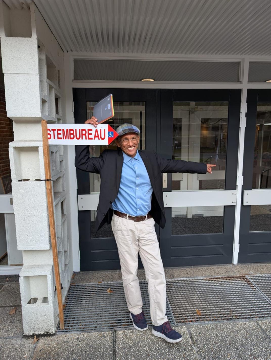 Man staat naast bordje met een pijl die wijst naar in de ingang van een stembureau