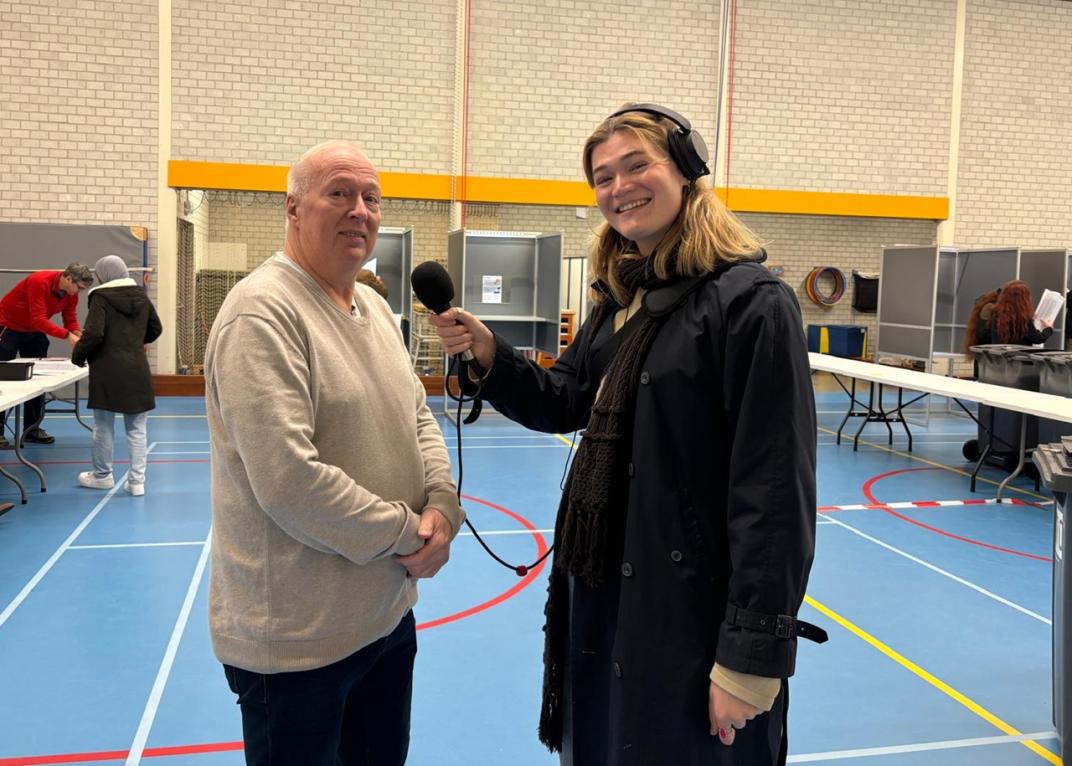 Student houdt microfoon voor de voorzitter van het stembureau in een interview