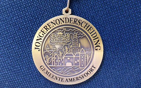 Een jongerenonderscheiding; een goudkleurige ronde hanger met daarop in reliëf de Koppelpoort