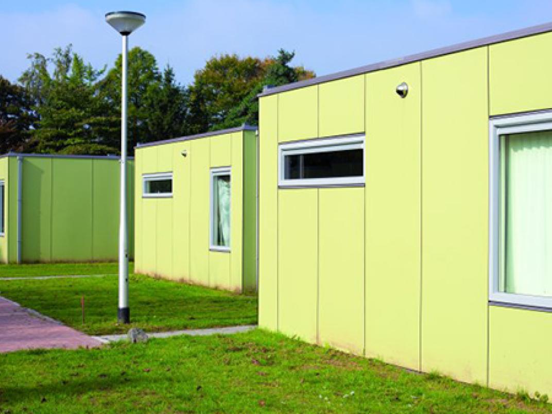 Skaeve Huse Tilburg;  een groep kleine gele gebouwen met grastuintjes.