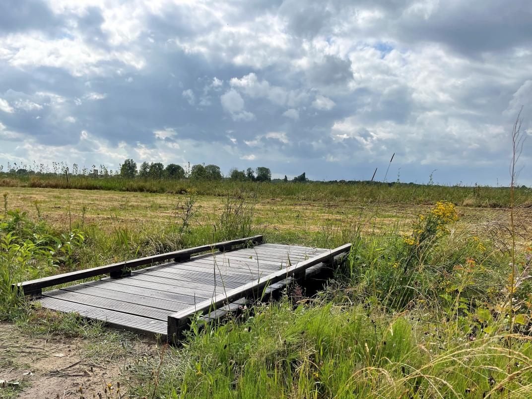 Foto van een groen landschap met een houten brug over een rivier