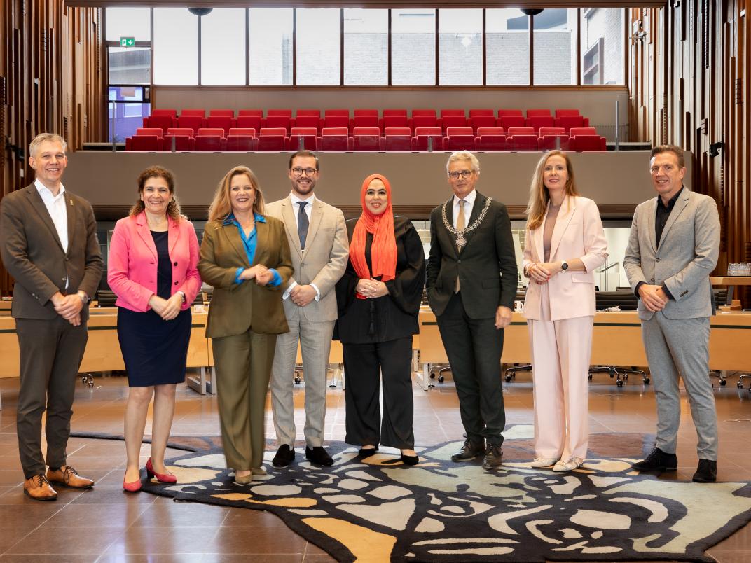 De leden van het College samen met de gemeentesecretaris staan in de raadszaal van het stadhuis
